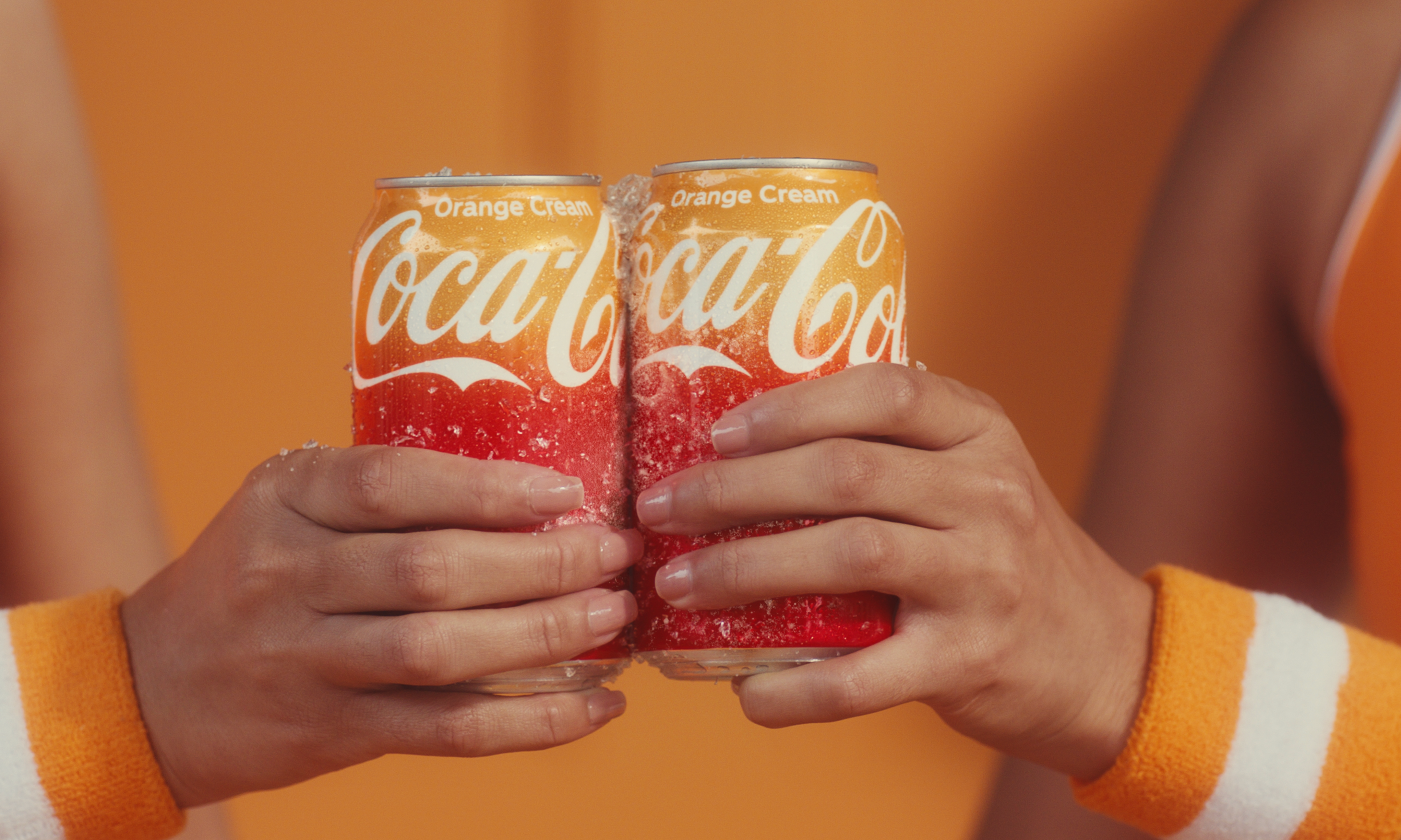 Two people holding cans of Coca-Cola Orange Cream