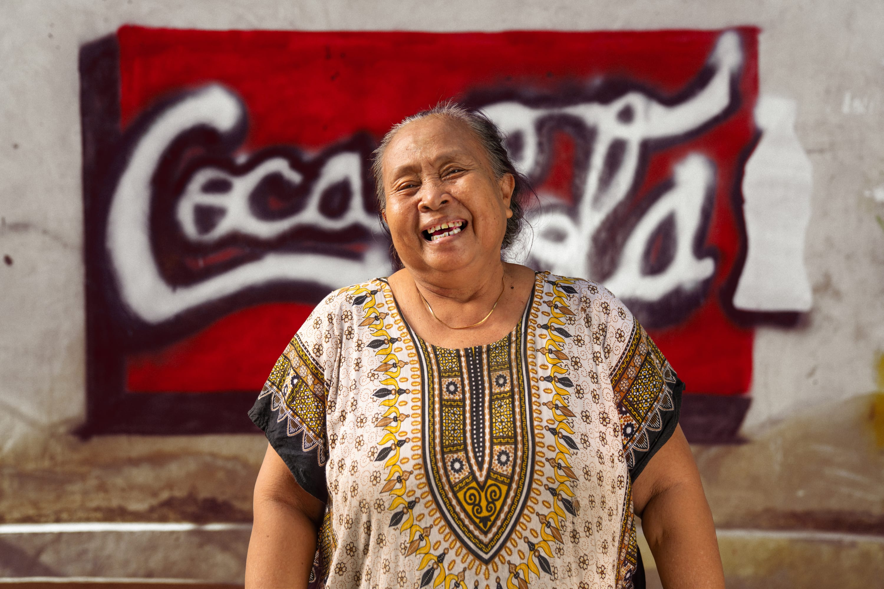 Woman smiling in front of spray painted unofficial Coca-Cola logo